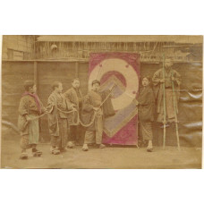 Boys holding rope by flag, one on stilts.