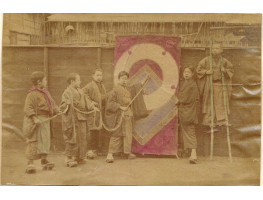 Boys holding rope by flag, one on stilts.