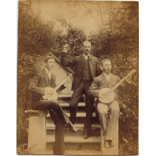 Photograph of two Banjo players seated on outdoor staircase, with another man standing playing the castanets.